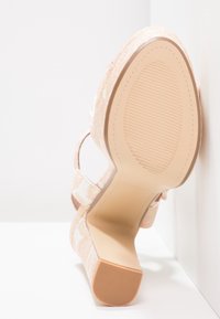 High-heeled sandal with textured sole and pink floral fabric, positioned sole-up against a white corner surface.
