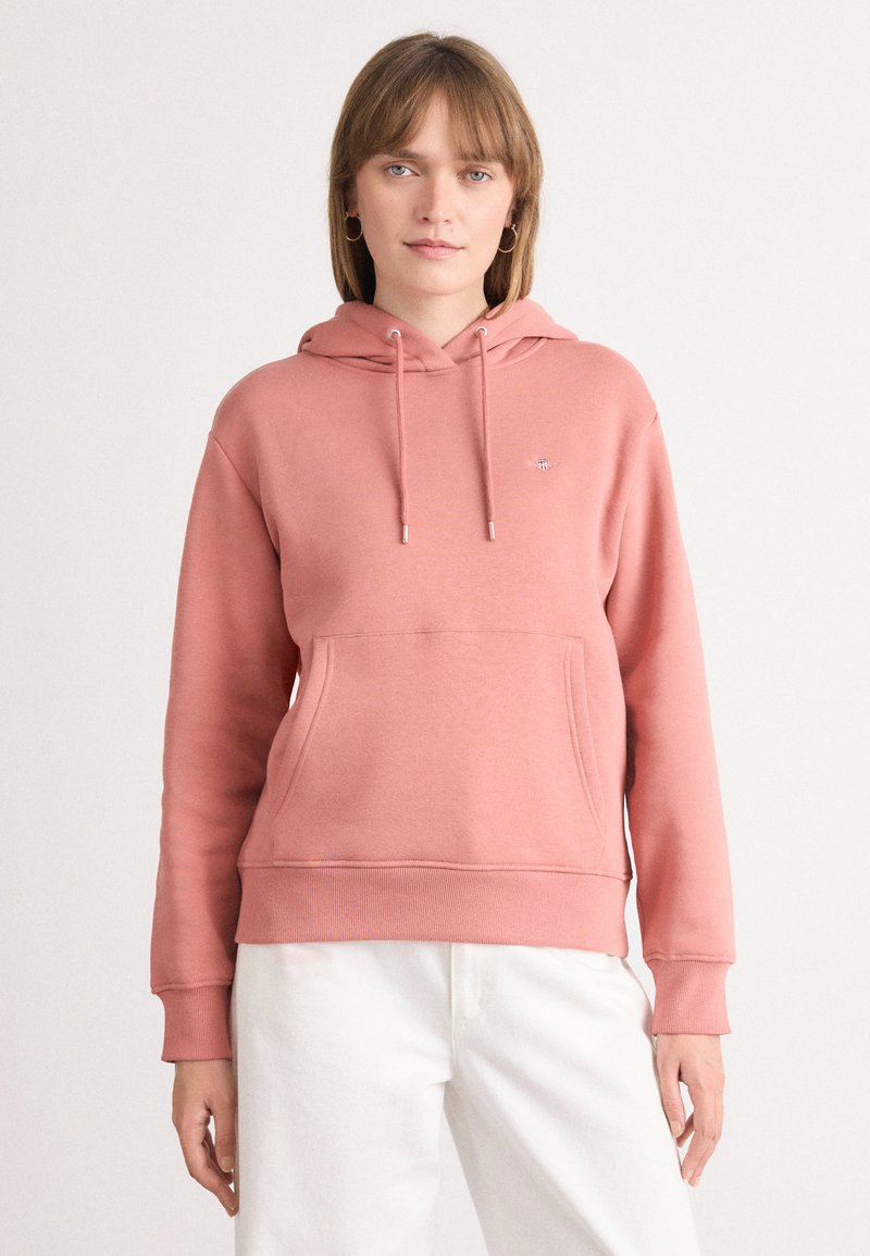Felpa rosa con cappuccio, tasca anteriore e polsini a coste. Lacci argentati e un piccolo dettaglio del logo vicino al petto.