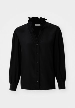 Svart bluse med volangdetaljer ved V-halsen, lange puffermer og knappelukking. Laget av glatt stoff med en lett glans.