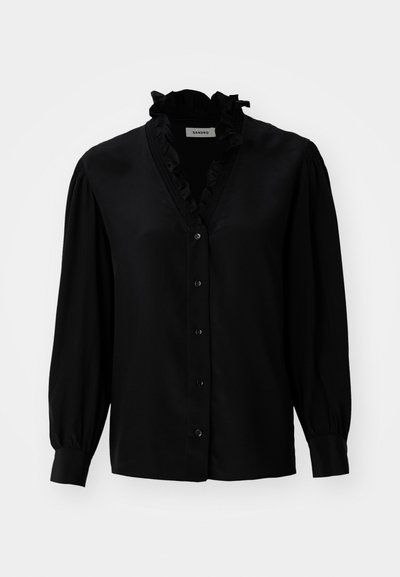 Svart bluse med volangdetaljer ved V-halsen, lange puffermer og knappelukking. Laget av glatt stoff med en lett glans.