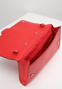 Sac à main en cuir rouge à texture lisse, doté d'une fermeture à pression magnétique et d'une poche intérieure zippée, présenté ouvert sur une surface blanche.