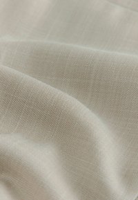 Svetlo bež tkanina s fino teksturiranim tkanjem, ki vsebuje subtilne barvne odtenke in gladko, mehko površino.