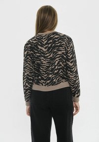 Suéter de rayas de tigre negro y beige con un dobladillo y puños acanalados, visto desde la parte posterior, combinado con pantalones de mezclilla oscuros.