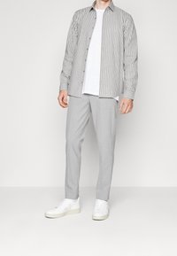 Camisa de botones a rayas en gris y blanco, combinada con pantalones grises claros y zapatillas blancas; tejido suave con un corte relajado.