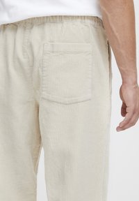 Pantalon en velours côtelé beige avec des ridules verticales, doté d'une poche arrière unique et d'une ceinture élastique, vu de profil droit.