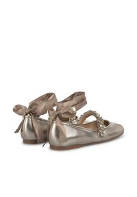 Ballerines métalliques dorées avec une semelle plate, ornement en bijou décoratif et lacets en satin autour de la cheville. Texture lisse et brillante.
