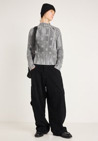 Γκρι πλεκτό πουλόβερ με ανάγλυφα αστέρια, σε συνδυασμό με υπερμεγέθη μαύρο παντελόνι από κοτλέ και μαύρα παπούτσια. Το μοντέλο φοράει μαύρο σκουφί.