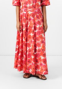 Maxikleid mit floralem Muster in Rot- und Rosa-Tönen. Hergestellt aus leichtem Stoff, mit kurzen Ärmeln, elastischem Bund und fließender Silhouette.