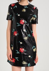 Robe noire en sequins avec manches courtes, broderie florale en rouge, jaune et vert. Encolure ronde et silhouette cintrée. Texture lisse.