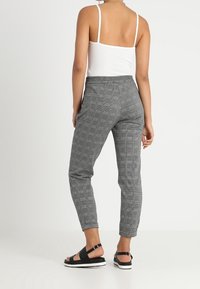 Kostkované šedé kalhoty s volným střihem, elastickým pasem a zúženými nohavicemi. Doplněné o černé sandály s páskovým designem.