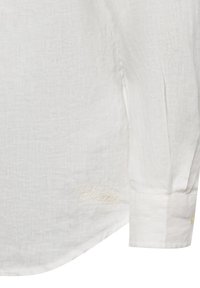 White linen shirt with long sleeves, featuring a subtle texture and a small embroidered label near the hem. Classic fit and rounded hemline.