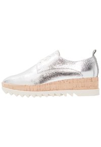 Chaussure argentée métallisée avec une tige texturée, une semelle intermédiaire en liège et une semelle en caoutchouc blanche à dents. Présente des lacets et un onglet au talon.