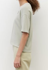 T-shirt in cotone grigio chiaro con una vestibilità comoda, collezione girocollo e maniche corte. Presenta cuciture visibili e un sottile dettaglio del logo.