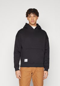 Black hooded sweatshirt with a front pocket and label detail at the bottom. Features a relaxed fit and soft texture.
