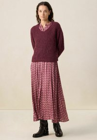 Pull en maille bordeaux avec un col en V, associé à une robe longue à motifs floraux dans des tons de rose et de violet, et des bottines noires.