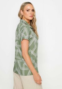 Korte mouwen groene shirt met een geometrisch wit patroon, met kraagontwerp, zachte stof en rechte zoom. Gestyled met beige broek.