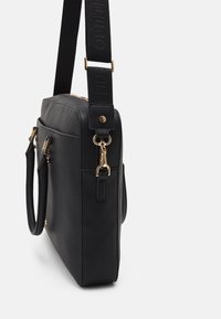 Mustan suorakulmaisen käsilaukun valmistettu teksturoidusta materiaalista. Siinä on kullanväriset metalliosat, pitkä olkahihna ja kaksi yläkahvaa.