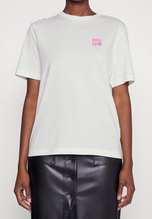 Person trägt ein weißes T-Shirt mit rosa „HUG“-Schriftzug und Herz auf der Brust, kombiniert mit einem schwarzen Lederrock mit Knopfleiste vorne.