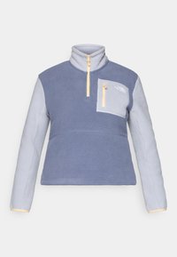 Fleece pulóver v svetlom modrom a šedom, s vysokým golierom, zipsom, prednou kapsou a kontrastnými žltými akcentmi.