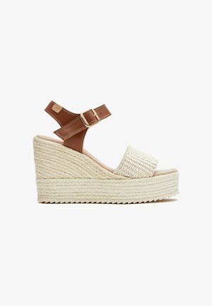 Sandalia cuña con plataforma de yute trenzado, tira para los dedos de color beige y correa de tobillo de cuero marrón con hebilla dorada, sobre fondo blanco.