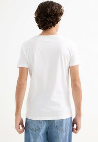 Camiseta blanca de manga corta con cuello redondo, textura suave y corte holgado, combinada con unos jeans de denim azul claro.