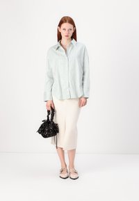 Lys grønn og hvitstripet oversized skjorte, kremfarget skjørt med splitt, svart blomsterhåndveske, og beige sko med detaljerte stropper.