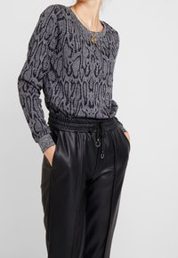 Maglione grigio a fantasia con collo rotondo e maniche lunghe; abbinato a pantaloni in ecopelle neri con tasche laterali e vita regolabile.