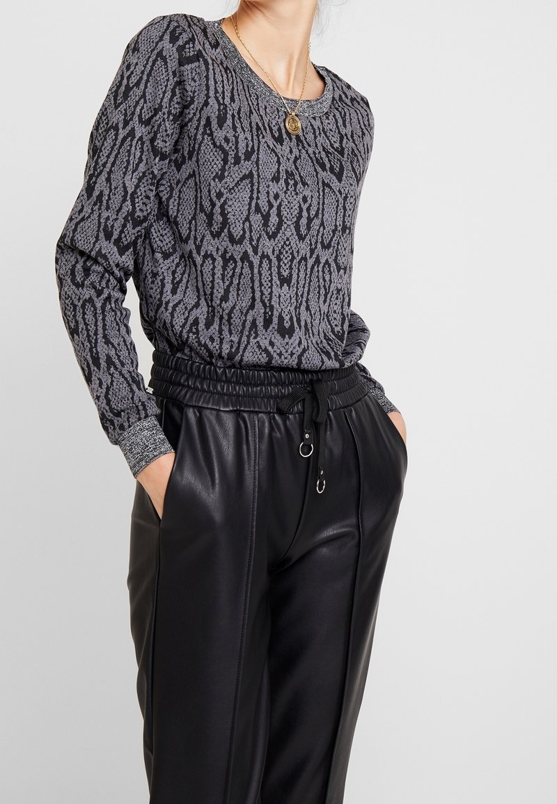 Maglione grigio a fantasia con collo rotondo e maniche lunghe; abbinato a pantaloni in ecopelle neri con tasche laterali e vita regolabile.