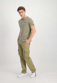 Khaki t-shirt with short sleeves and a small logo, paired with khaki cargo pants featuring multiple pockets, worn with white sneakers.