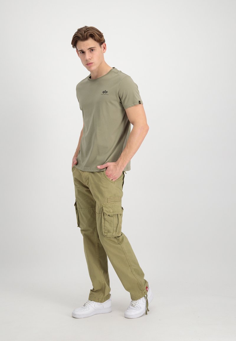 Khaki T-Shirt mit kurzen Ärmeln und kleinem Logo, kombiniert mit khakifarbenen Cargo-Hosen mit mehreren Taschen, getragen mit weißen Sneakers.