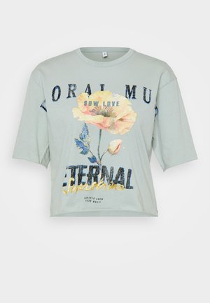 Camiseta de algodón verde claro con un corte holgado, mangas cortas, estampado gráfico floral y texto que dice "SIEMBRA AMOR SOL ETERNO."