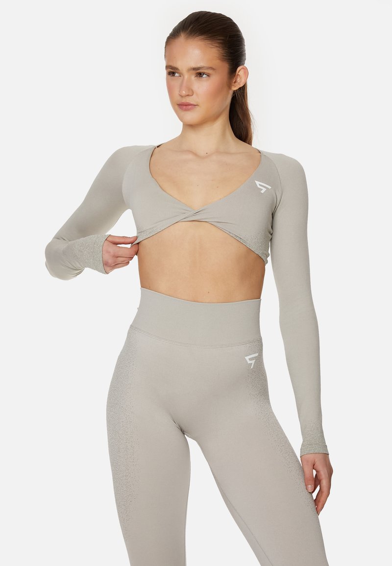 Hellgraues, langärmliges, gekürztes Oberteil mit V-Ausschnitt und einem Twist-Design, kombiniert mit hochtaillierten Leggings, die eine dezente Farbverlaufstextur aufweisen.