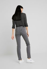 Jeans gris de corte ajustado con una cintura de altura media, que cuentan con bolsillos traseros y detalles de costura sutiles, combinados con una camiseta de manga larga oscura y zapatillas blancas.