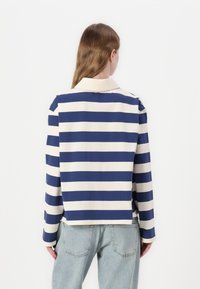 Striped long-sleeve shirt in navy and cream, featuring a collar, dropped shoulders, and a relaxed fit. Made from soft fabric with a smooth texture.