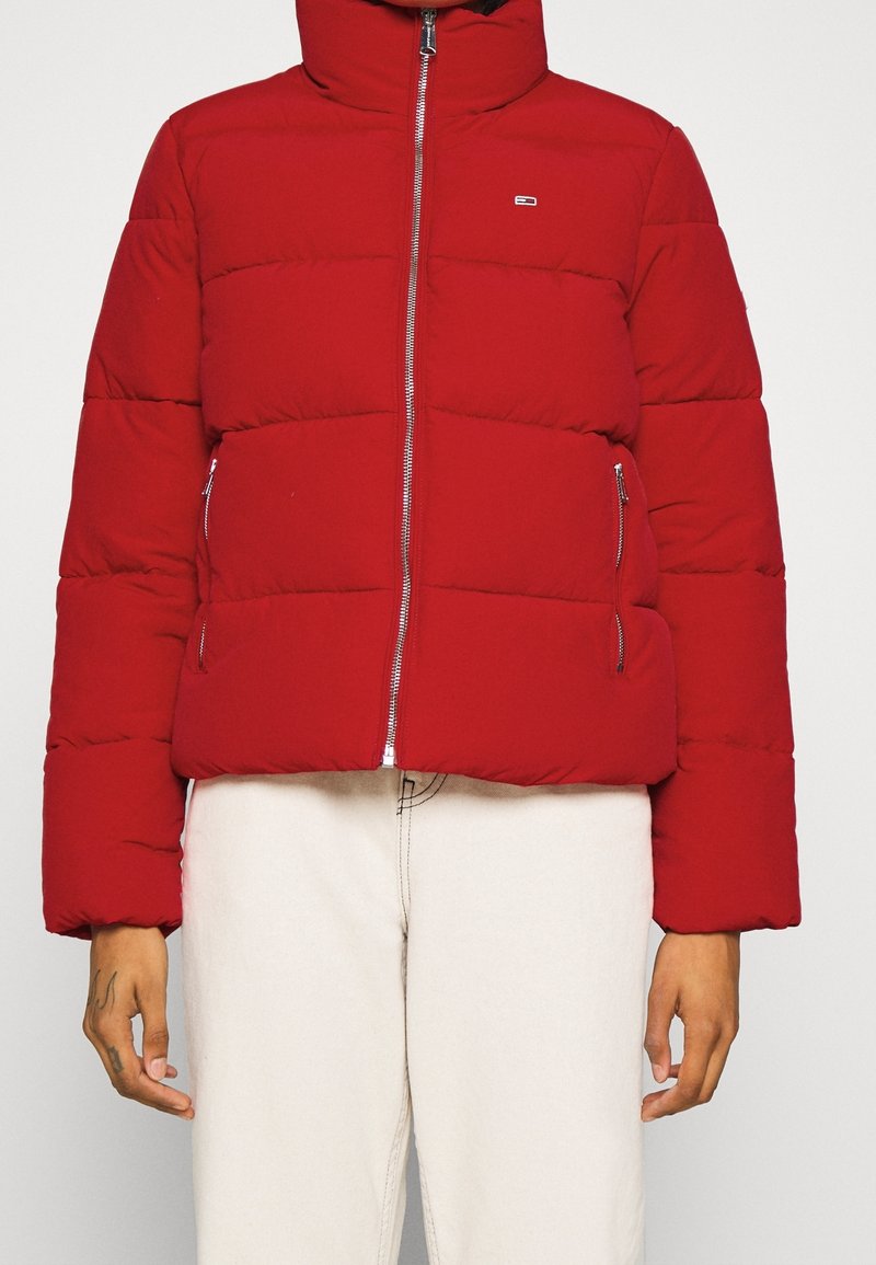 Giacca imbottita rossa con colletto alto, design a righe orizzontali, zip frontale e due tasche laterali. Texture morbida e materiale caldo.