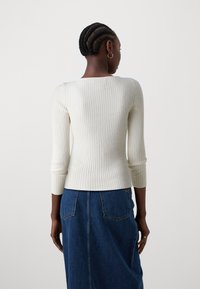 Biały, prążkowany top z długim rękawem i kwadratowym dekoltem, zestawiony z niebieską spódnicą dżinsową z tylnymi kieszeniami i detalami przeszyć.