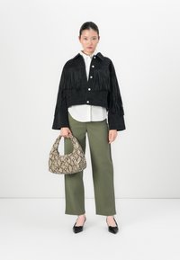 Giacca di jeans nera con frange, camicia bianca a bottoni, pantaloni verdi oliva e borsa a stampa serpente, completata con scarpe flat nere.