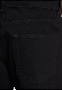 Jean en denim noir avec une poche arrière ornée d'un détail de couture subtil. Le tissu a une texture lisse et une couleur uniforme sans ornements.