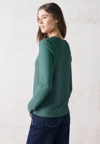 Grön randig långärmad topp med rund halsringning, texturerat tyg, i kombination med mörka denimbyxor. Enkelt mönster, avslappnad stil.