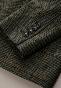 Tweed jacket sleeve with brown and green check pattern, featuring four dark brown buttons in a row near the cuff.