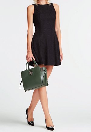 Robe noire sans manches en dentelle, sac à main en cuir vert avec logo, et escarpins noirs avec accents décoratifs. Design simple et élégant.