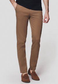 Chinos wąskie brązowe o gładkiej teksturze, z szlufkami na pasek i bocznymi kieszeniami, w połączeniu z brązowymi loafersami. Tkanina wydaje się lekka i trwała.