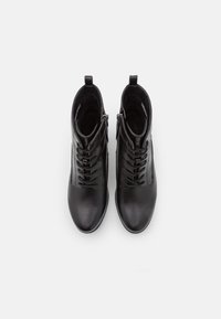 Mustad mustad nahast pahkluupid jalatsid ümmarguse varbaga, paeltega esiosaga ja külgmise lukuga. Sile tekstuur, õmblusdetailid ja minimalistik disain.