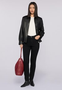 Chaqueta de cuero negra con cuello tipo camisa, top blanco, jeans de mezclilla negros y botas negras estilo tobillo. Sosteniendo un bolso de cuero rojo.