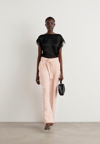 Blusa di satin nera con maniche corte, pantaloni rosa chiaro con vita legata e una piccola borsa nera strutturata. Tacchi grigi completano l'outfit.