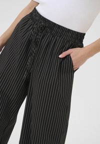 Black pinstriped pants with an elastic waistband, drawstring, and side pockets, featuring a smooth texture and straight-leg design.