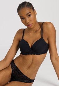 Svart bh med släta kupor och spetsdekoration, i kombination med matchande spetsunderbyxor. Justerbara axelband och sömlös design för komfort och stöd.