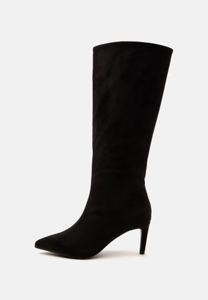 Botte noire en daim montant jusqu'au genou avec un bout pointu et un talon fin de hauteur moyenne sur un fond clair uni.
