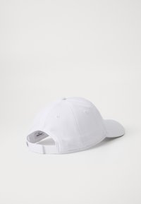 Fehér baseballsapka textúrált anyagból, ívelt karimával és hátul állítható pánttal. A tetején szellőzőnyílásokkal rendelkezik.