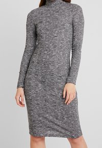 Harmaa pitkähihainen mekko, jossa on korkea kaulus, teksturoitu kuvio ja vartalonmyötäinen leikkaus, ulottuen polviin.